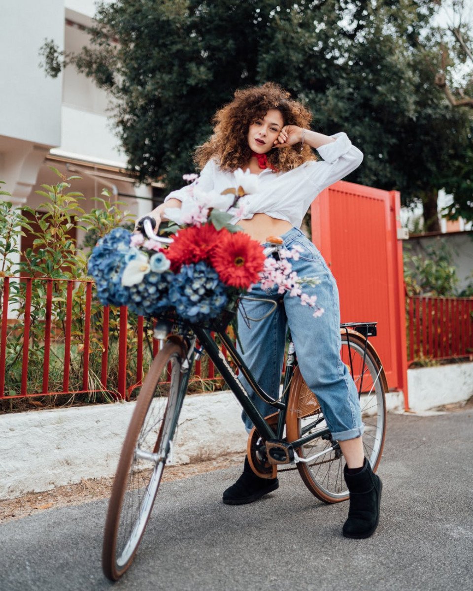 woman in white long sleeve shirt and blue denim jeans standing with bicycle on road